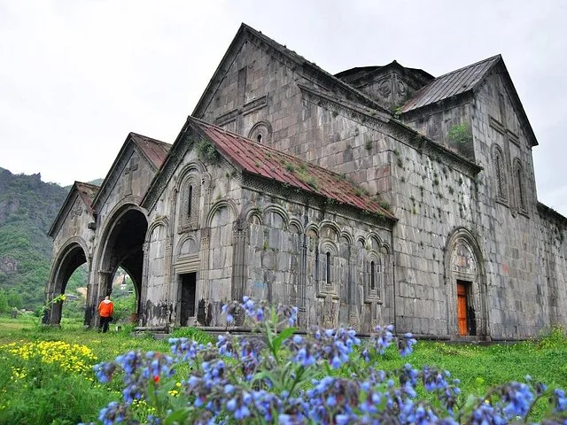 Die steinerne Fassade des Klosters Haghpat, gesehen von einem Feld mit lila Wildblumen.