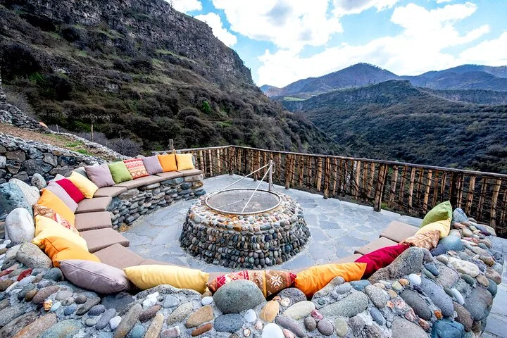 Outdoor seating area with colorful cushions overlooking a scenic mountainous valley landscape.