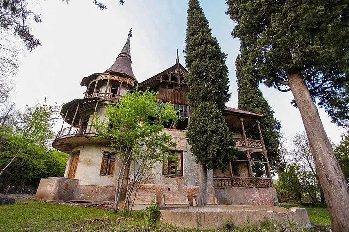 Old, abandoned multi-story building with ornate wooden balconies surrounded by trees.