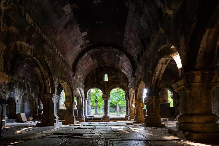 Interior of Haghpat Monastery featuring stone pillars and arches illuminated by sunlight.