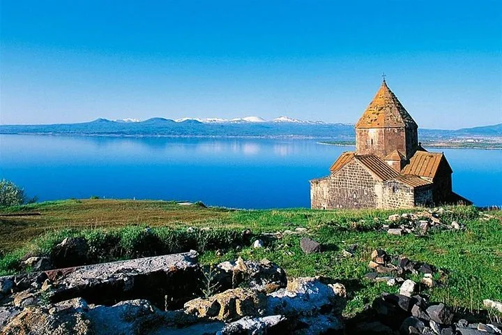 Scenic view of a stone monastery overlooking a bright blue mountain lake.